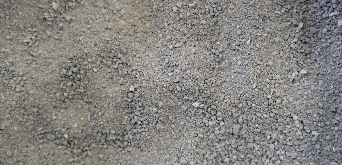 Image : poudre de roche grossièrement à finement granulée, gris moyen et étalée sur une surface plane