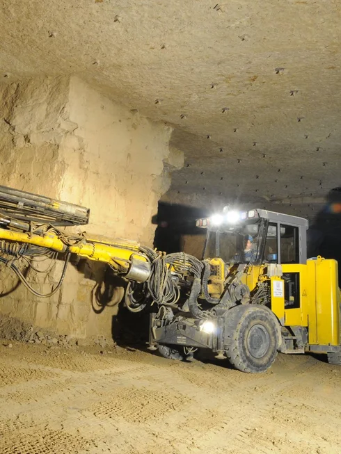 Foto: Grubenfahrzeug untertage mit langem Ausleger, an dem ein Bohrer in die Grubenwand gefĂŒhrt wird
