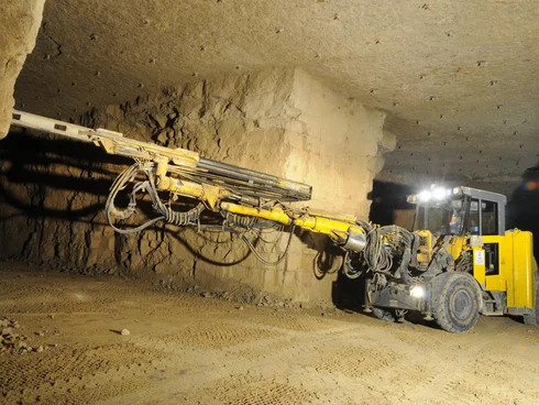 Foto: Grubenfahrzeug untertage mit langem Ausleger, an dem ein Bohrer in die Grubenwand geführt wird