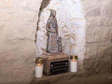 Foto: Steinskulptur der Heilige Barbara unter einem gemauerten Steinbogen; links und rechts zwei Kerzen