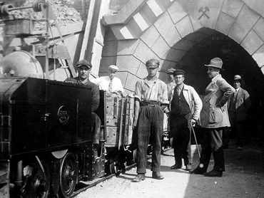 Image historique : Des mineurs posent à côté du train minier et du portail d’une mine où est inscrit « Franz H. Hansen Stollen 1925 » (Galerie Franz H. Hansen Stollen 1925).